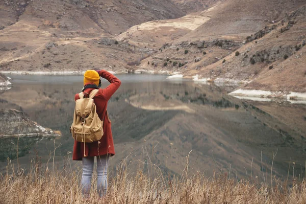 Um retrato da parte de trás de uma menina viajante tirar uma foto no fundo de um lago nas montanhas no outono ou início da primavera. Conceito de viagem — Fotografia de Stock