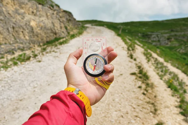 A mão masculina está segurando uma bússola magnética no fundo das colinas e o céu com nuvens. O conceito de viajar e encontrar o seu caminho de vida — Fotografia de Stock