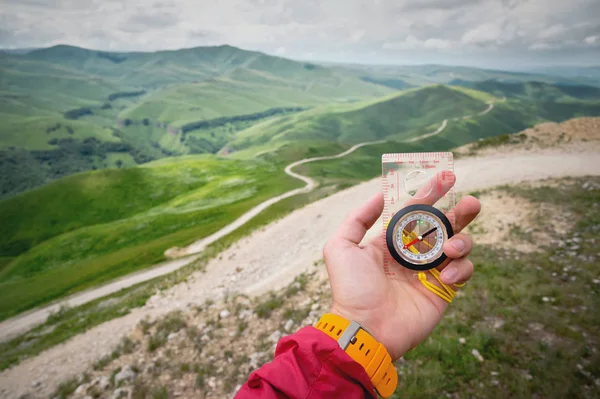 Male hand is holding a magnetic compass on the background of hills and the sky with clouds. The concept of traveling and finding your life path — Stock Photo, Image