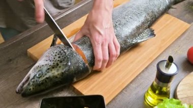 Eller Close-up büyük somon ev yemekleri, ahşap bir masa üzerinde bir bıçak ile kesme