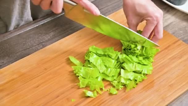Penutup tangan wanita mengiris daun salad hijau di papan kayu di dapur rumah. Konsep vegetarianisme dan makanan sehat — Stok Video