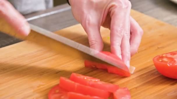 Close-up de mãos femininas com uma faca estão cortando tomates para fazer salada em uma placa de corte de madeira. Cozinha caseira. Alimentos saudáveis — Vídeo de Stock