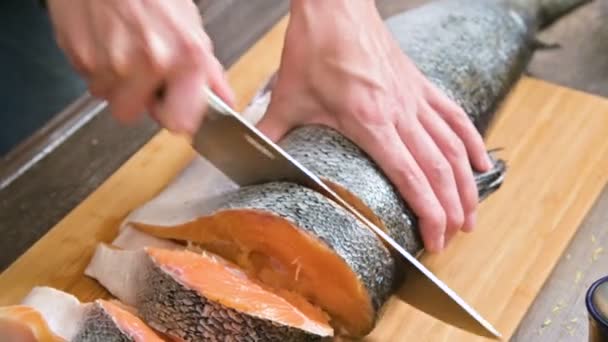 Close-up van vrouwelijke handen snijden met een mes een grote zalm op een houten tafel van thuis koken — Stockvideo