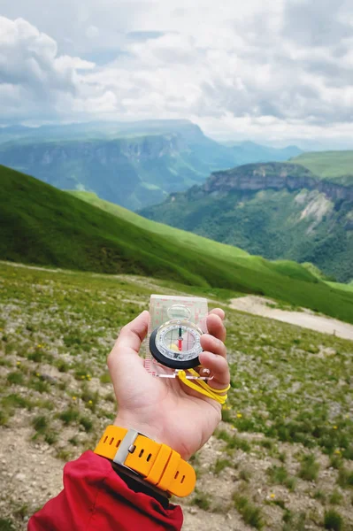 Male hand is holding a magnetic compass on the background of hills and the sky with clouds. The concept of traveling and finding your life path — Stock Photo, Image