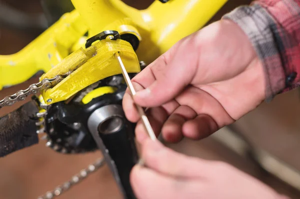 Close-up maintenance of a mountain bike. Male hands adjust the chain tension. Technical condition monitoring in the workshop