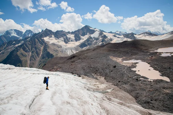 Een bergbeklimmer met een rugzak wandelingen in stijgijzers wandelen langs een stoffige gletsjer met trottoirs in handen tussen scheuren in de berg — Stockfoto