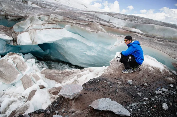 Il viaggiatore in berretto e occhiali da sole è seduto sulle montagne innevate sul ghiacciaio. Viaggiatore in un ambiente naturale — Foto Stock