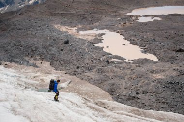 Bir sırt çantası ile bir dağcı çatlaklar dağ arasında elinde kaldırımlar ile tozlu bir buzul boyunca yürüyüş krampon içeri girer