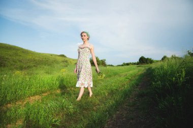 bir buket ile alaca elbiseli Genç mutlu gülümseyen kız olan yeşil çimen ülke yol boyunca yürüyüş