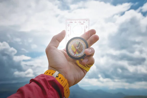 男性の手は、雲と空の背景に磁気コンパスを保持しています。旅行とあなたの人生のパスを見つけることの概念 — ストック写真