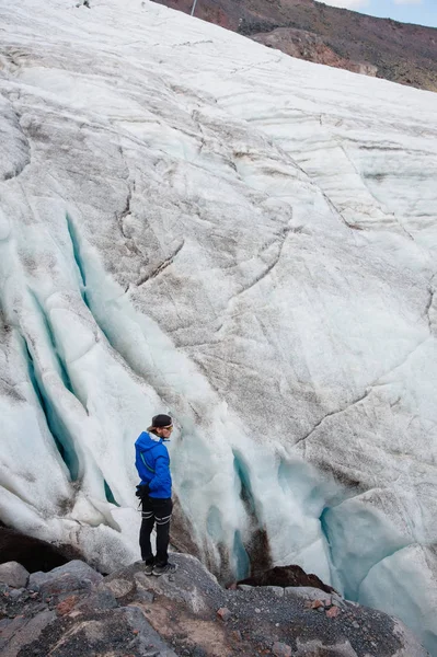 Reiziger in een pet en zonnebril staat in de besneeuwde bergen op de gletsjer. Reiziger in een natuurlijke omgeving — Stockfoto