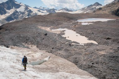 Bir sırt çantası ile bir dağcı çatlaklar dağ arasında elinde kaldırımlar ile tozlu bir buzul boyunca yürüyüş krampon içeri girer