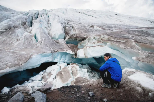 El viajero con gorra y gafas de sol está sentado en las montañas nevadas del glaciar. Viajero en un entorno natural —  Fotos de Stock