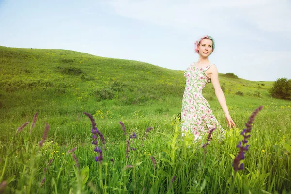 Jong gelukkig lachend meisje in een calico jurk met een boeket loopt langs een landweg met groen gras — Stockfoto