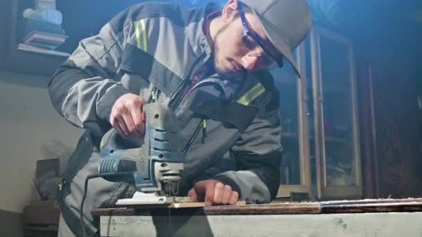 Gri tulum ve gözlük mesleği sakallı genç adam bir marangoz bir elektrikli testere onun ev atölye olarak çalışıyor. Kesme ahşap parçaları — Stok video