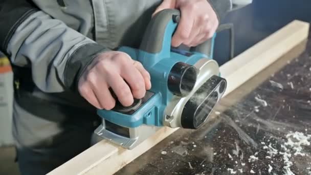 Primer plano de la mano de un carpintero que trabaja con un plano eléctrico en un taller doméstico. Acabado de piezas de madera — Vídeos de Stock