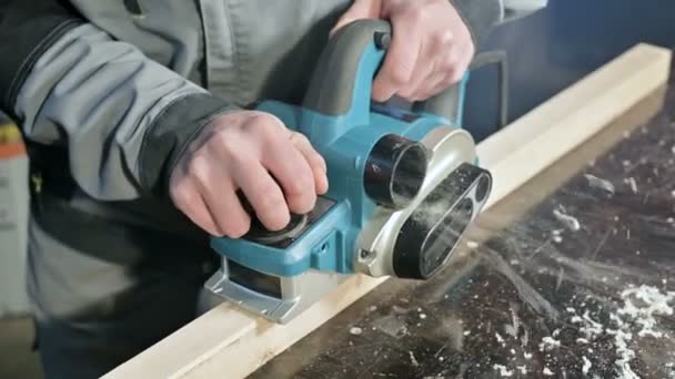 Primer plano de la mano de un carpintero que trabaja con un plano eléctrico en un taller doméstico. Acabado de piezas de madera — Vídeo de stock