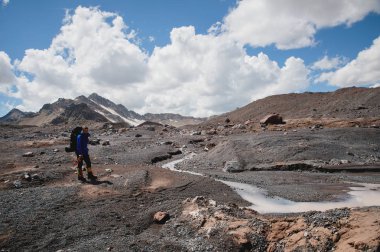 Bir sırt çantası ile bir dağcı çatlaklar dağ arasında elinde kaldırımlar ile tozlu bir buzul boyunca yürüyüş krampon içeri girer