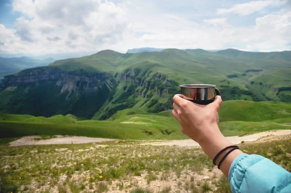 Vista en primera persona de una mano de las niñas sosteniendo una taza de té de plástico contra una meseta de colinas verdes y un cielo nublado en verano — Foto de Stock