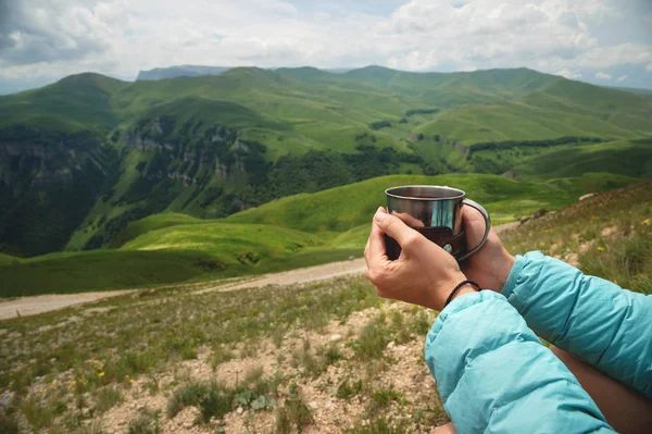 First-person view of a girls hands holding a plastic cup of tea against a plateau of green hills and a cloudy sky in summer — Stock Photo, Image