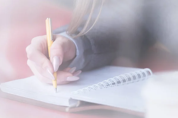 Gros plan d'une étudiante dans un café derrière le verre avec un reflet qui écrit quelque chose avec un stylo à bille dans un carnet. Contraste pour la réflexion — Photo