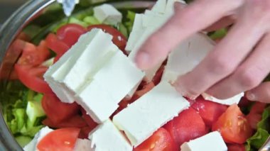 Kadın şef el Yunan vegan domates salatası zeytin ve marul yaprakları beyaz peynir küpleri koyarak kapatın. Sağlıklı beslenme ve yaşam tarzı kavramı