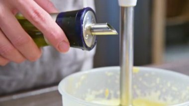 Plastik bir kabın içinde bir blender ile ev yapımı mayonez karışımını çırpma yakın çekim. zeytin yağı