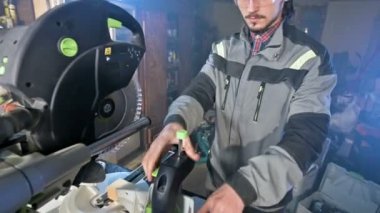 Genç bir marangoz ahşap bir iş parçası bir dairesel testere makinesinde yükler. Home atölye. Acemi işadamı
