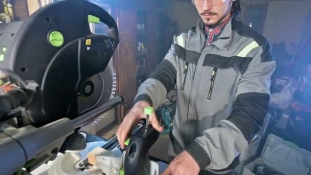Un joven carpintero instala una pieza de madera en una serradora circular. Taller casero. Empresario novato — Vídeos de Stock
