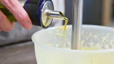 Plastik bir kabın içinde bir blender ile ev yapımı mayonez karışımını çırpma yakın çekim. zeytin yağı