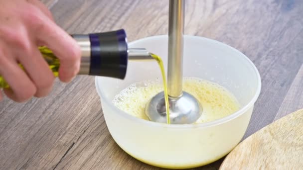 Крупным планом взбивая смесь домашнего майонеза с блендером в пластиковой миске. оливковое масло — стоковое видео