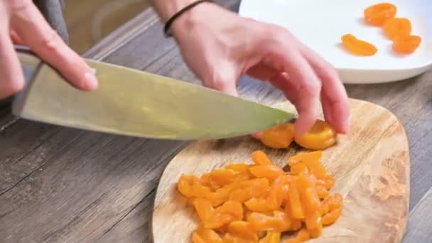 Primer plano de las manos femeninas cortando albaricoques secos con un cuchillo en una tabla de cortar. Cocinar comida vegetariana — Vídeo de stock