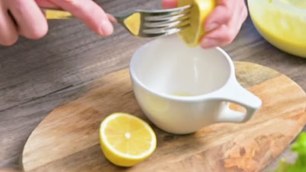 Närbild av kvinnliga händer pressa en citron i en mugg på en skärbräda i hemmet köket — Stockvideo