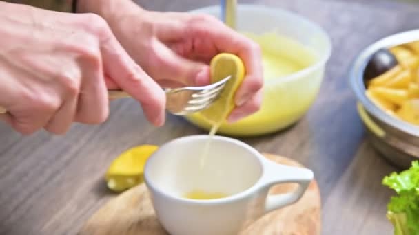 女性の手のクローズ アップが家庭の台所でまな板の上のマグカップにレモンを絞る — ストック動画