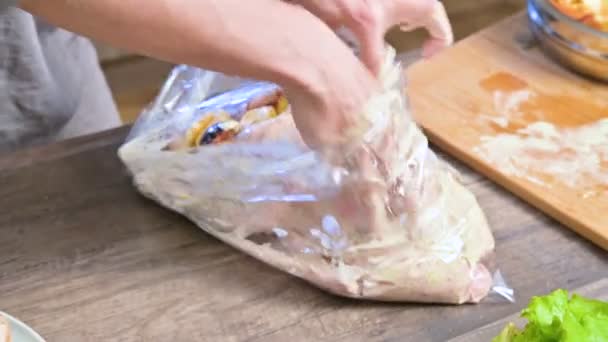 Close-up female hands are wrapped in a plastic bag with a duck or a goose for baking. White dressing with mayonnaise. Christmas goose duck with apples — Stock Video