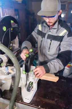 Genç bir erkek marangoz bir iş parçası dairesel bir makineye yükler. İşlemeli. Bir iş kurma