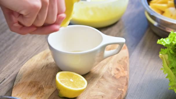 Primer plano de las manos femeninas exprimir un limón en una taza en una tabla de cortar en la cocina del hogar — Vídeos de Stock