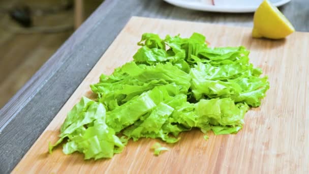 Penutup tangan wanita mengiris daun salad hijau di papan kayu di dapur rumah. Konsep vegetarianisme dan makanan sehat — Stok Video