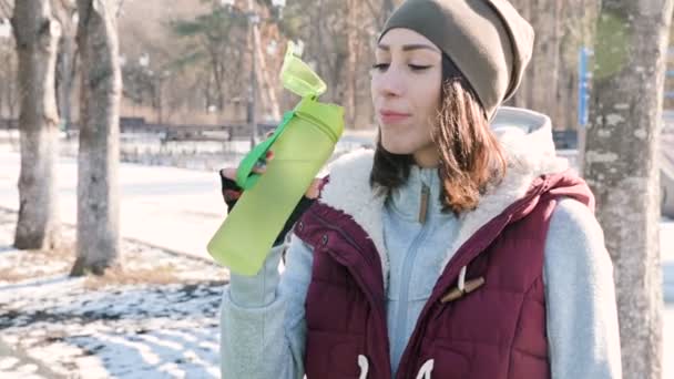 Sportovní holka na venkovní trénink v parku na sportovní hřiště v zimě na slunečný den pitné vody z šejkru — Stock video