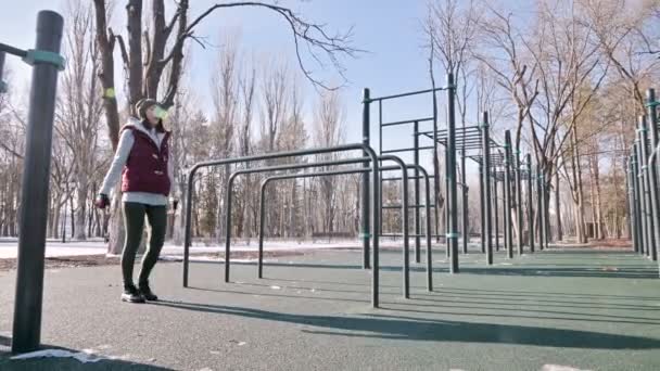 Ângulo baixo contra o sol. Menina de esportes no inverno no playground faz lunges avançando . — Vídeo de Stock
