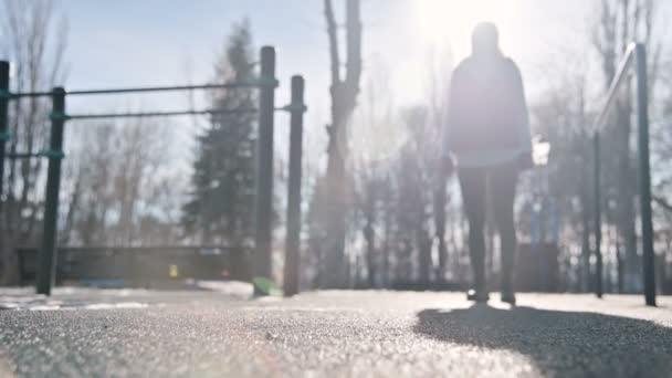 Низкий угол против солнца. Спортивная девушка зимой на детской площадке делает выпады шагая вперед . — стоковое видео