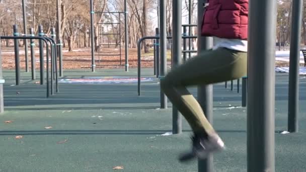 Close-up of girls legs on the open area for workout. Woman shakes the press hanging on the horizontal bar. — Stock Footage Close Girls Legs Open Area Workout Woman Shakes Press Hanging Stock Video