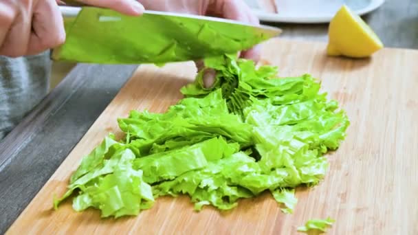 Primer plano de las manos femeninas rebanando hojas de ensalada verde en una tabla de madera en una cocina casera. Concepto de vegetarianismo y comida saludable — Vídeo de stock