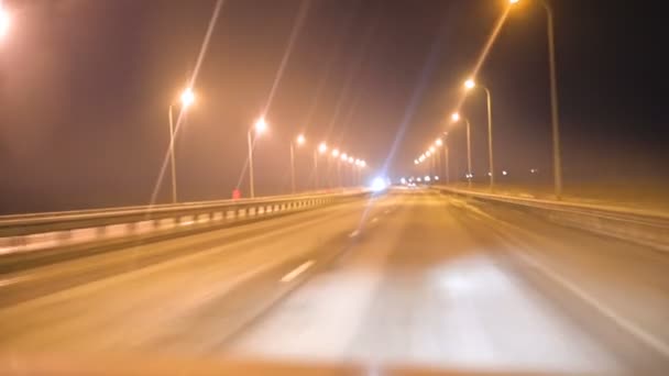 Het uitzicht vanuit de auto door de voorruit van de auto op de avond track met verlichting lampen. Nacht snelweg — Stockvideo