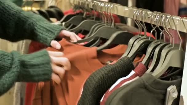 Крупный план руки девушки в магазине, выбирающей одежду, висящую на вешалках для продажи — стоковое видео