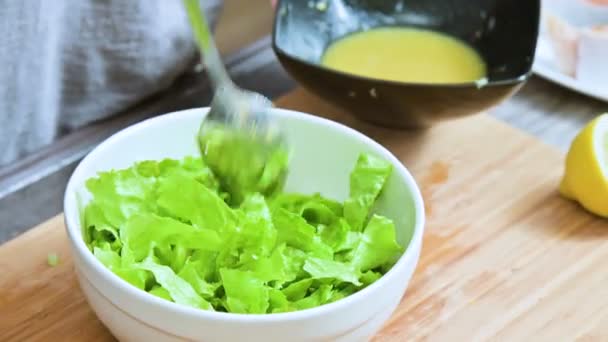 Close-up of female hands in a home kitchen are added to a vegetarian leaf salad sauce and mixed with a spoon on a wooden cutting board — Stock Video