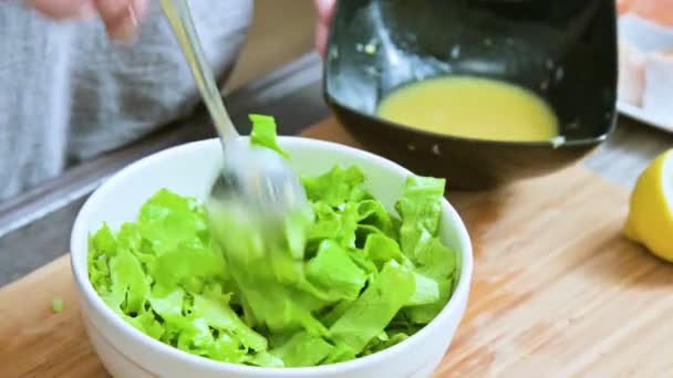 Pendekatan tangan perempuan di dapur rumah ditambahkan pada saus salad daun vegetarian dan dicampur dengan sendok pada papan potong kayu — Stok Video