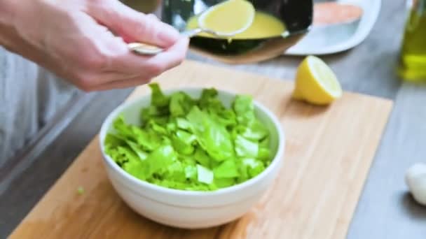 在家庭厨房里, 女性手的特写镜头被添加到素食叶子沙拉酱上, 并与木制切菜板上的勺子混合 — 图库视频影像