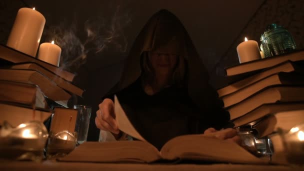 Medelstora närbild flicka trollkarl med huva i ett mörkt rum med levande ljus och letar efter en spell som välter en bok. Lågmäld. Mystic små Dof — Stockvideo