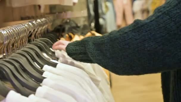 Primer plano de una mano de las niñas en una tienda elegir la ropa que cuelga de perchas para la venta — Vídeos de Stock